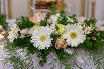 Delicate white daisies and soft pink roses create a stunning centerpiece, enhancing the ambience of a joyful gathering. Lush greenery frames the arrangement, adding vibrancy and life.