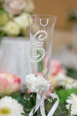 A stunning wedding toast glass sparkles with intricate pearl designs and sits among a lush arrangement of fresh flowers. The elegant decor captures the essence of romance and celebration.