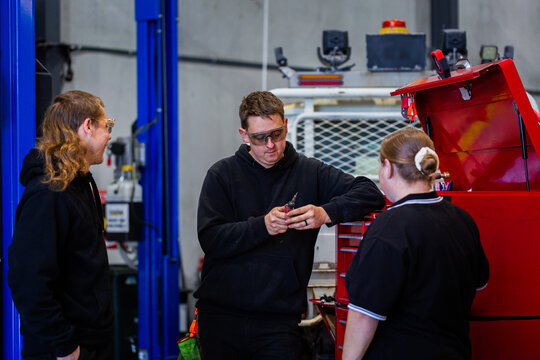 two mechanics in repair workshop chatting together with woman by toolbox cabinet