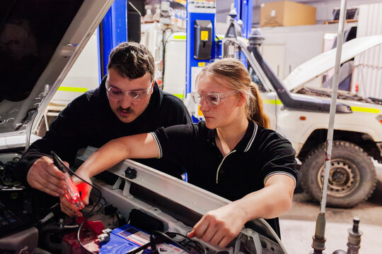 female mechanic tradeswoman working on car repair in industrial workshop with supervisor