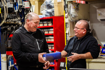 Two older aussie men working in parts section of mechanics workshop talking together