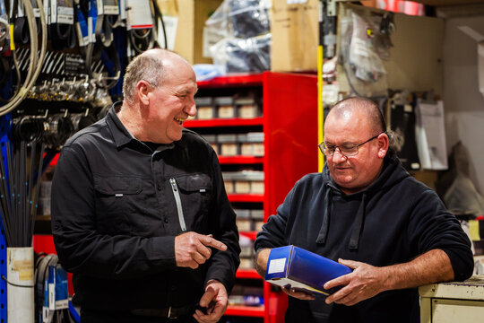 Two older aussie men working in parts section of mechanics workshop talking together