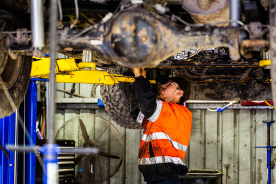 young aussie mechanic worker working on repairs under vehicle in workshop wearing orange high-vis