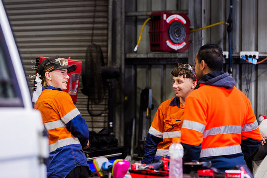 Three Australian men in industrial mechanics shed workplace chatting in conversation together