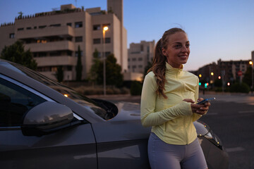 Sportswoman using smartphone leaning on her car at sunset