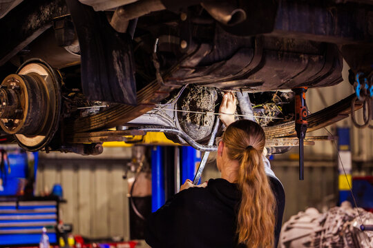 Female mechanic working on differential axel component underneath vehicle