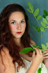 Selective focus sensual portrait of beautiful young woman with dark red wavy hair holding a leafy...
