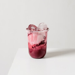 Iced red velvet milk with creamy swirl and ice in a clear cup, photographed on white background....