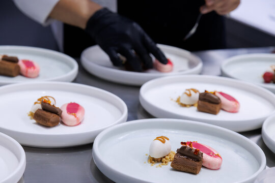 plated desserts in professional restaurant kitchen. chef arranges chocolate cake, mousse, and artistic garnishes on plates. fine dining presentation, culinary art and gourmet food preparation.