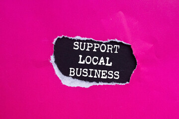 Support local business message written on ripped torn pink paper on black background. Conceptual...