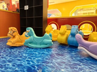 Colorful plastic rocking horses lined up on a floor designed to look like rippling water in a bright, indoor play area.