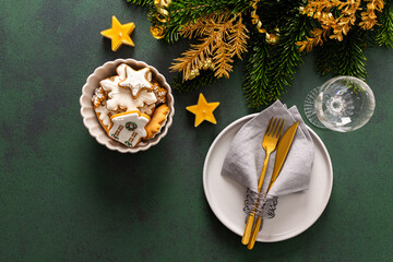 A festive table setting with an empty plate, napkin and cutlery and gingerbread on a green...