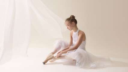 The beauty behind perfection. Elegant ballerina sitting and adjusting pointe shoes. Concept of discipline, beauty, dance rituals, lifestyle, focus, and feminine strength.