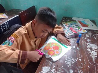 A young student diligently cuts out a colorful paper design at his desk in the classroom.