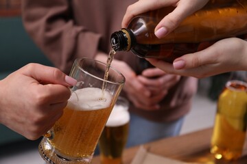 Woman pouring beer into her friend's glass indoors, closeup