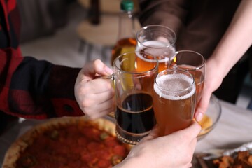 Friends clinking glasses of beer at white wooden table, closeup