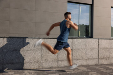 Fototapeta premium Man in sportswear running near building outdoors, motion blue effect
