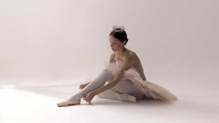 Ballerina in tutu adjusting pointe shoes with serene concentration. Concept of beauty, discipline, ritual, femininity, inner strength, and mindful preparation in performance.