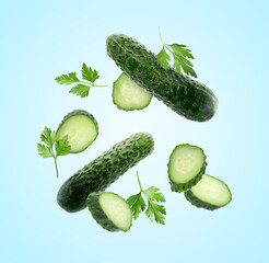 Fresh cucumbers and parsley falling against light blue background