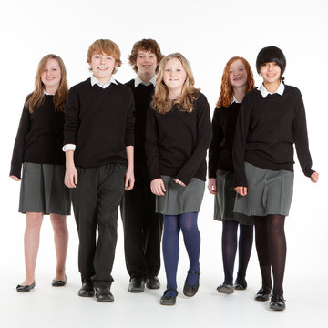 Secondary School: A group of six early teenage children in school uniform standing together and smiling at the camera. Full length studio shot on a white background. From a series of images.