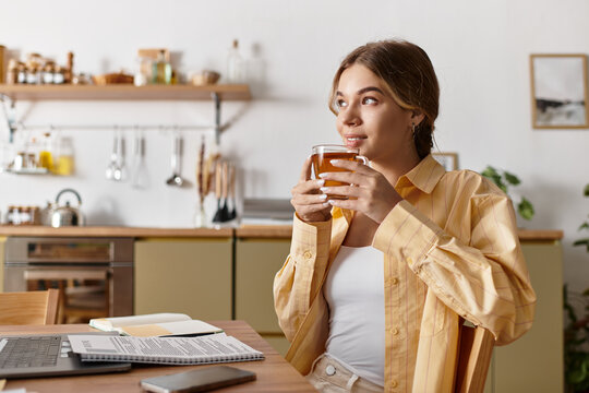 Beautiful young woman sits comfortably at home sipping tea and gazing thoughtfully out the window.