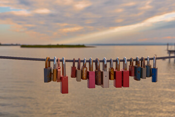 Colorful padlocks symbolizing love on a fence by Lake Neusiedl, Austria, with vibrant pastel sunset reflecting on tranquil waters.