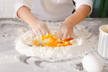 The hands of a little girl in white t-shirt making a dough with flour and eggs.