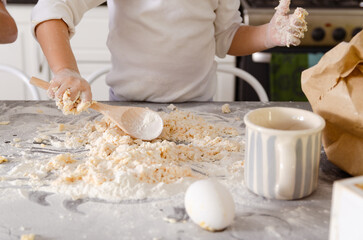 The hands of a little girl in white t-shirt cooking with a wooden spoon and dough. 