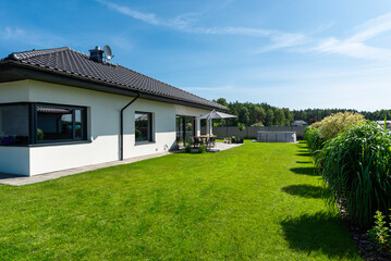 A beautiful garden with green grass, a patio table and umbrella visible, a house in beautiful...