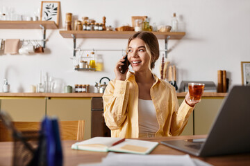 A young woman sits in her cozy home, chatting joyfully on the phone with a cup of tea in hand.