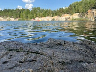 Calm water reflecting blue sky with green trees along rocky shore during sunny day in summer