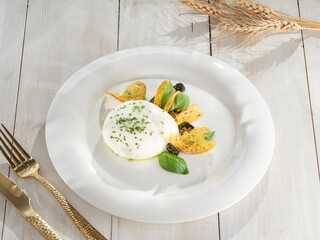 On a wooden table in bright sunlight, burrata rests on a white plate alongside crispy bread, basil,...