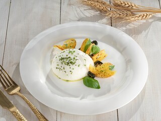 A pristine white plate holds a ball of creamy burrata, garnished with chives, basil leaves, golden...