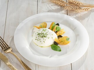 A fresh Burrata, generously sprinkled with chives, sits on a white plate surrounded by fried...
