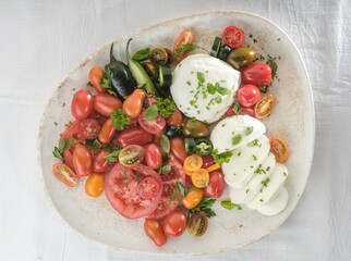 A colorful assortment of sliced heirloom tomatoes, Jalapeno peppers, and fresh mozzarella, adorned...