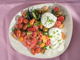 Colorful arrangement of heirloom tomatoes, fresh mozzarella, herbs, and jalapenos create a...