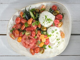 A colorful dish is presented with sliced heirloom tomatoes in shades of red, orange, and yellow,...