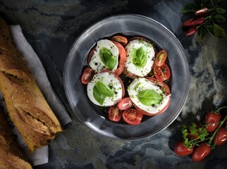 Caprese salad served on a pewter plate with fresh basil leaves, sliced cherry tomatoes, a drizzle...