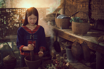 A smiling Asian woman cooks in the kitchen, sitting in a wicker basket in the garden of a rural home. A vintage image of the beauty of Isan, Thailand.