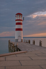 The Podersdorf Lighthouse rises over its own pier, glowing in soft evening light against a pastel sky on the shores of Neusiedler See in Austria’s Burgenland region. Calm waters and gentle colors crea
