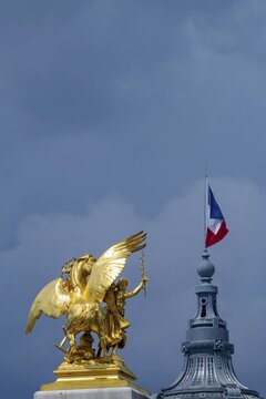 Column with the group of figures Fama of Agriculture on the Pont Alexandre III bridge over the Seine, behind it the dome of the Grand Palais with the French national flag, Tricoloe, Paris, &Icirc;le-de-France, France