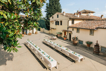 Aerial view of long rustic wedding tables. Romantic outdoor dinner in Tuscan villa courtyard. Italian event with eco style decor 