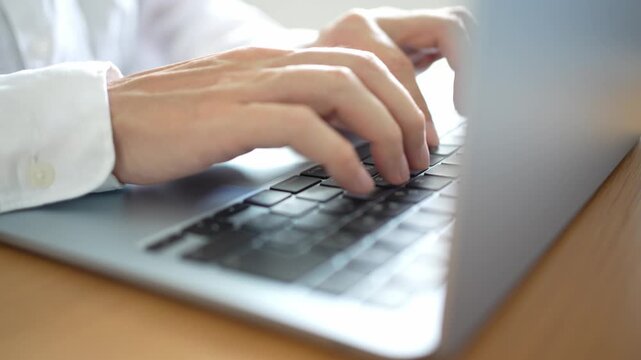 ノートパソコンでタイピングしている人の手。フリーランスのITエンジニアがリモートワークでおしゃれで清潔感のある自宅のデスクでプログラミングの仕事の作業をしているイメージ