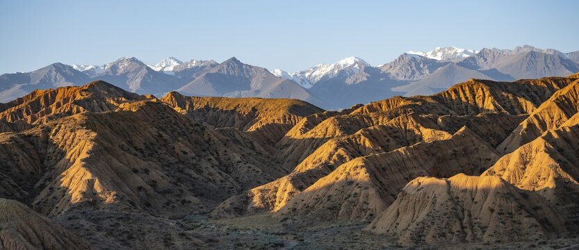 Landscape of eroded hills at sunrise, badlands, white mountain peaks of the Tian Shan Mountains in the background, Canyon of the Forgotten Rivers, Issyk Kul, Kyrgyzstan