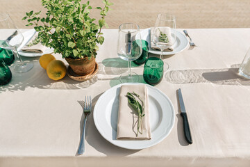 Eco wedding table decor with mint in old terracotta pot, lemons, wine glasses, green glassware and linen napkin