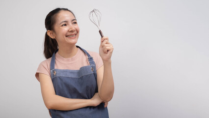 A smiling woman in an apron holds a whisk, ready to cook or bake, conveying enthusiasm and joy in...