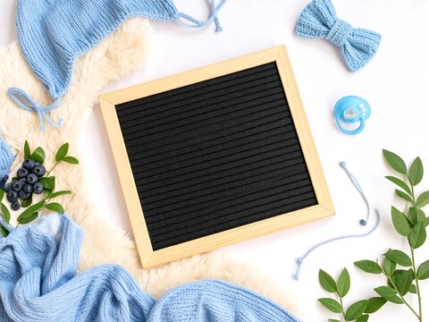 Baby boy announcement concept with blue clothes, a pacifier, and a blank letter board mockup for text. Flat lay composition for a newborn baby shower.