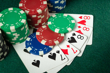Stacks of colorful poker chips are laid out next to playing cards depicting a full house or a full...