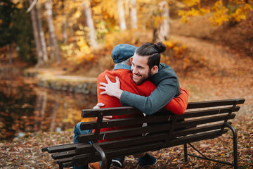 Fototapeta premium Grandad and grandson sitting on bench in park and hugging.