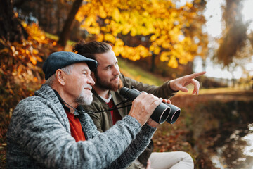 Senior father and his son with binoculars in nature, talking.